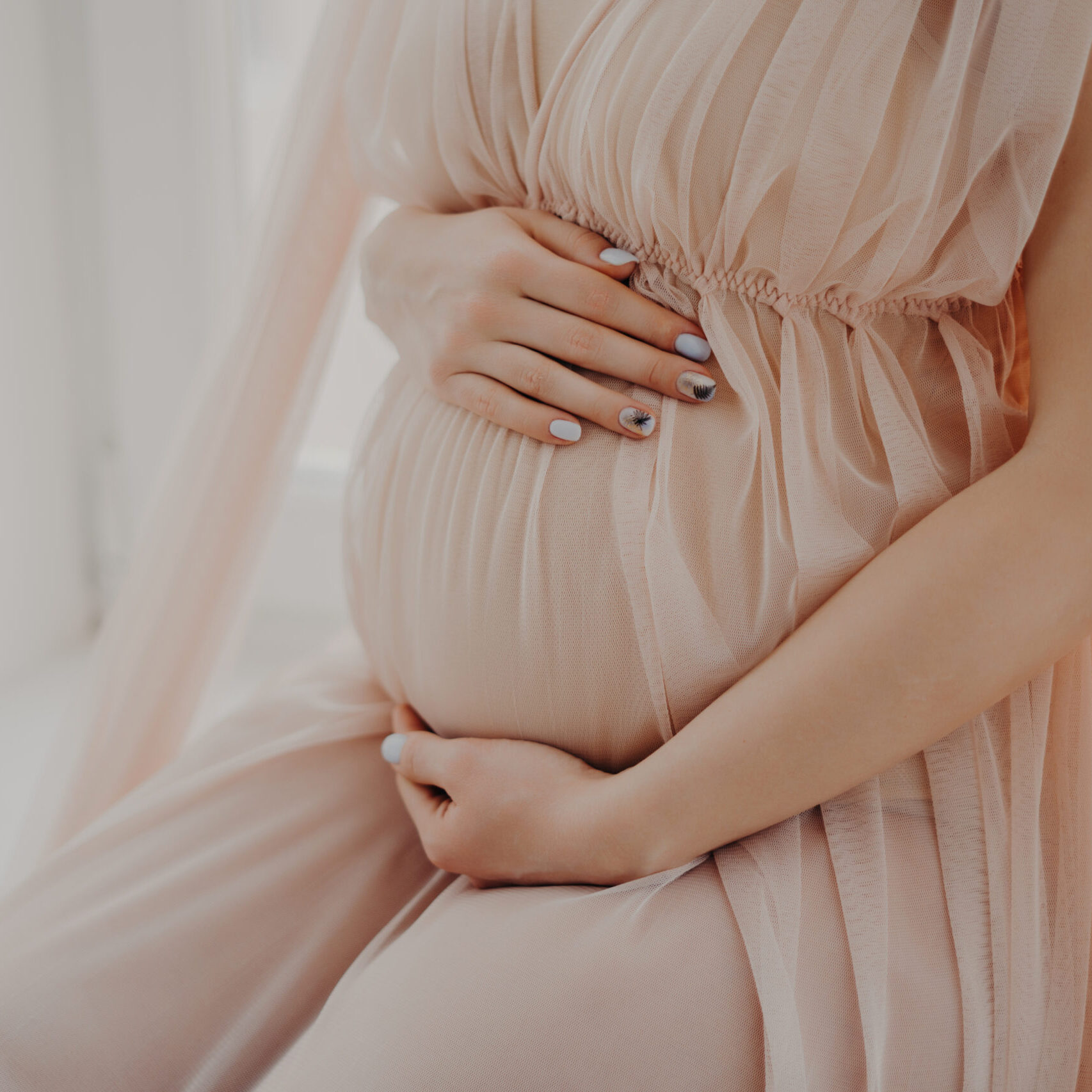 Cropped image of faceless woman touches her abdomen anticipates for baby wears festive dress poses indoor. Women and pregnancy concept